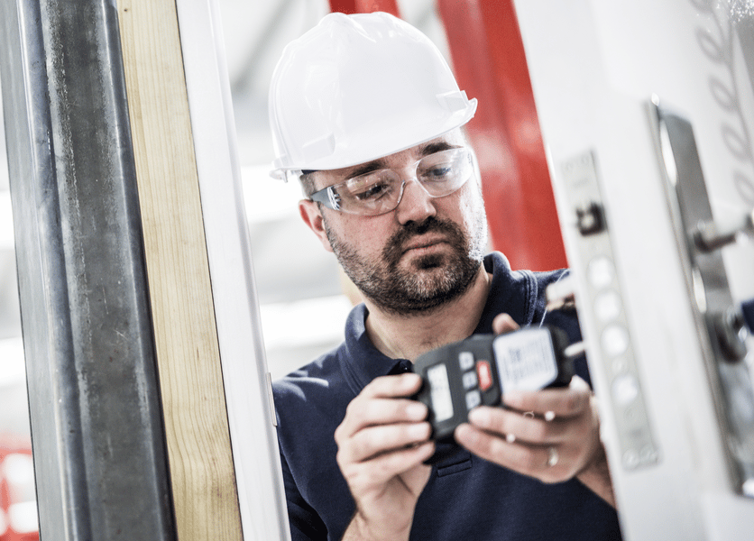Building products testing engineer in a hard hat studying the results of a testing meter while standing in a door frame